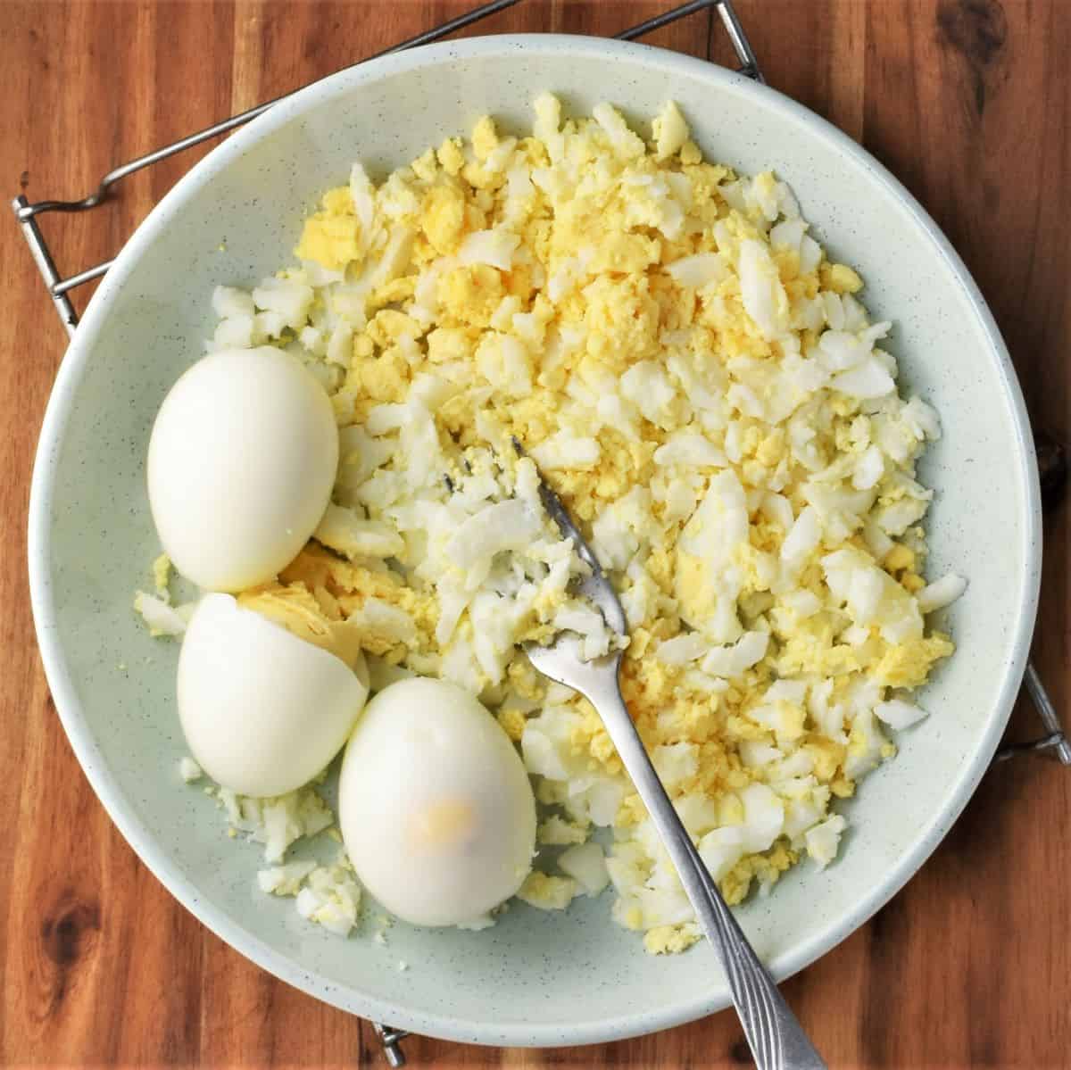 Mashing hard-boiled eggs with fork in bowl.