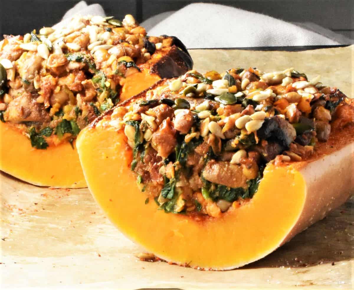 Side view of cut lentil stuffed butternut squash halves on top of parchment.