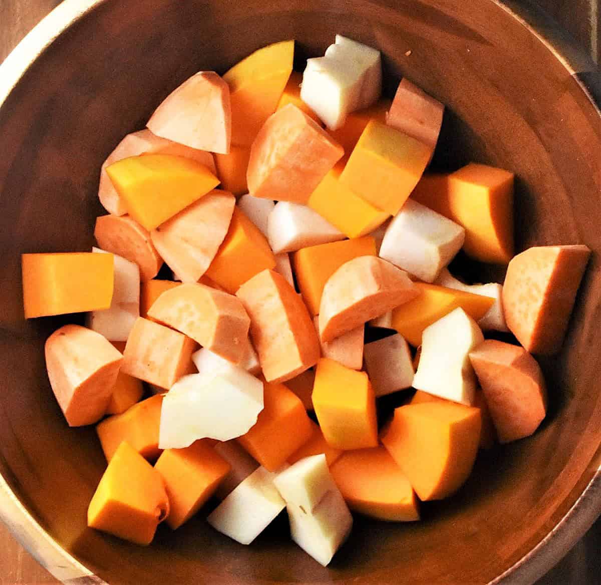 Top down view of large chunks of vegetables in wooden bowl.