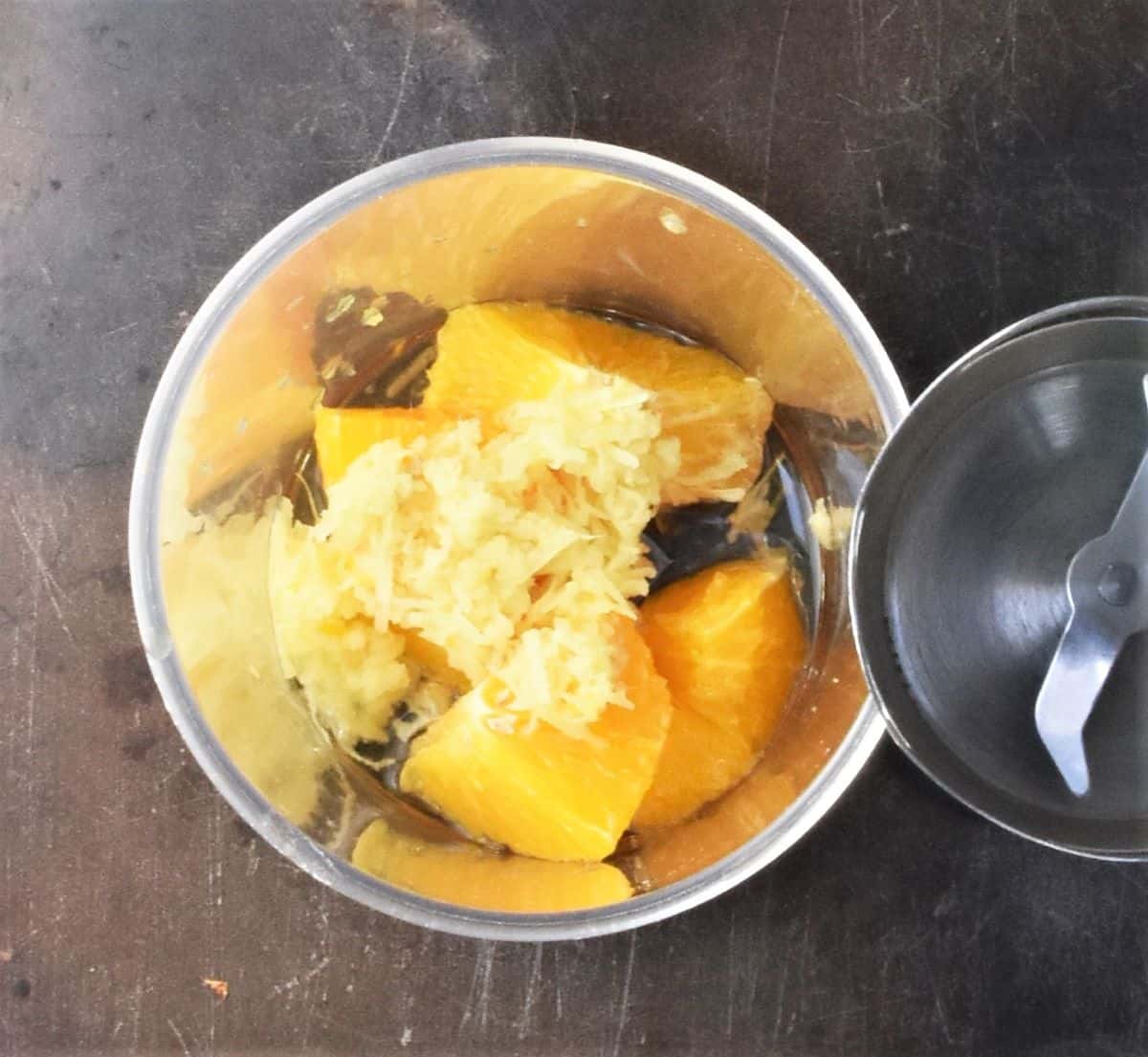 Orange chunks and ginger in tall glass with blender end to right.