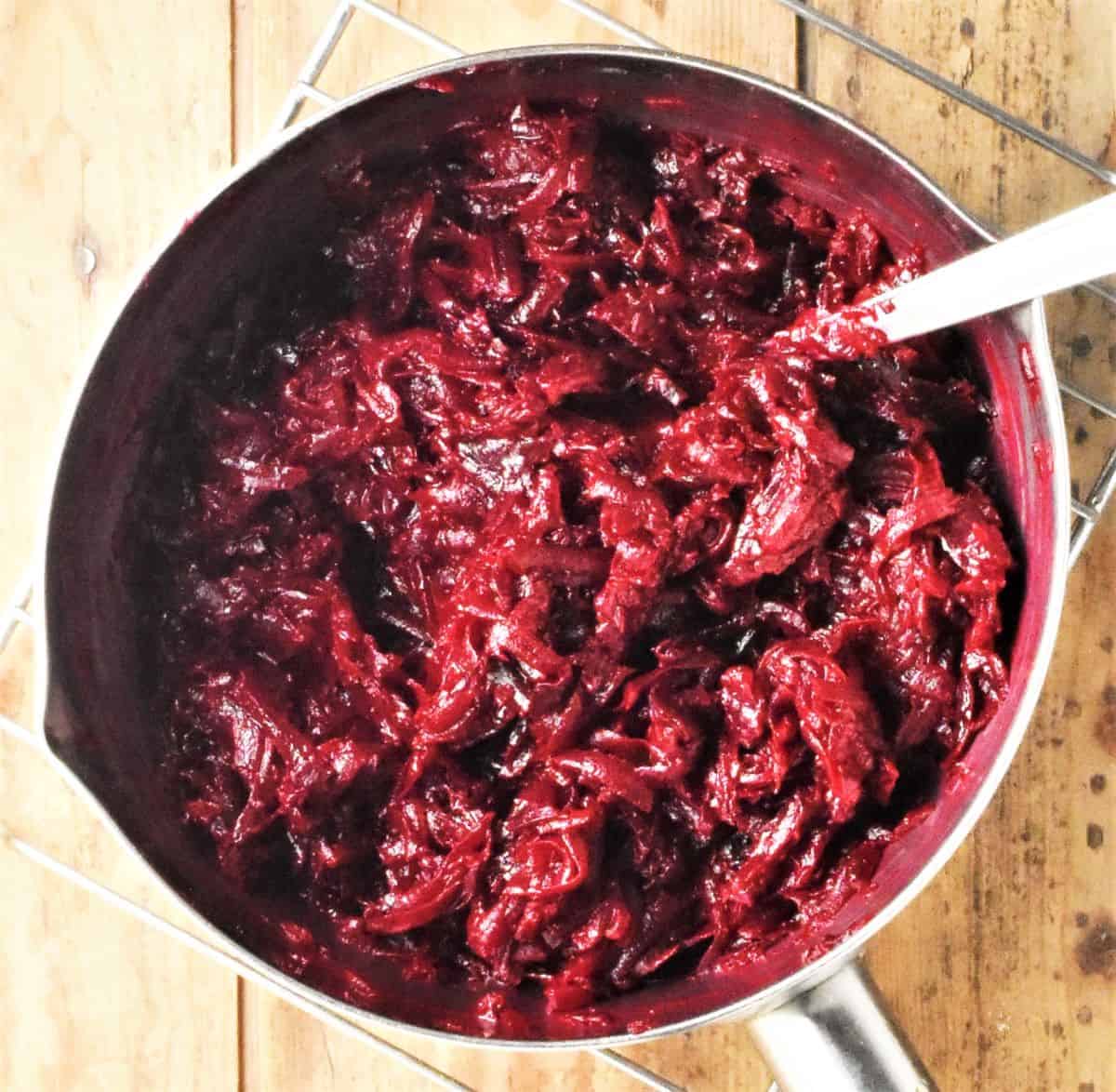 Cooking shredded beetroot in saucepan with spoon.