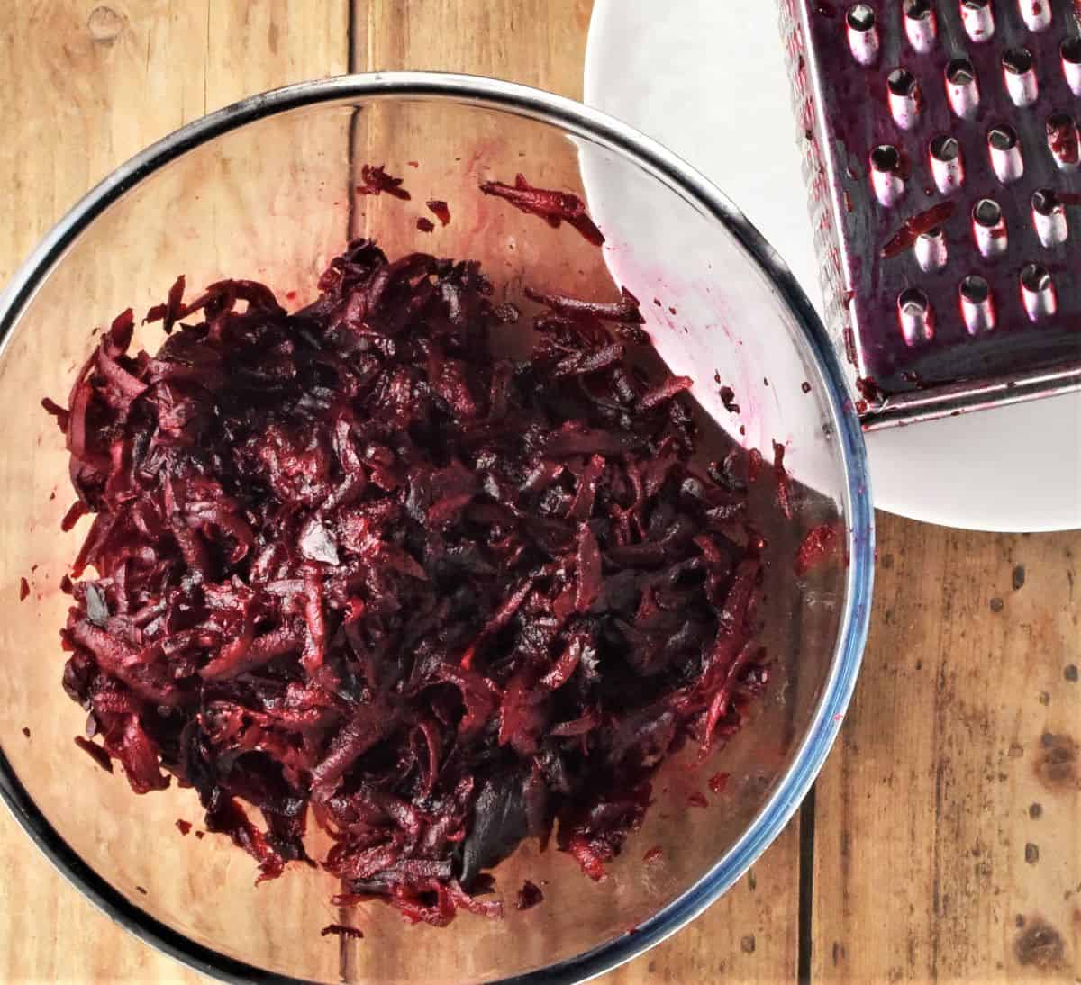 Top down view of grated beets in bowl with grater in background.