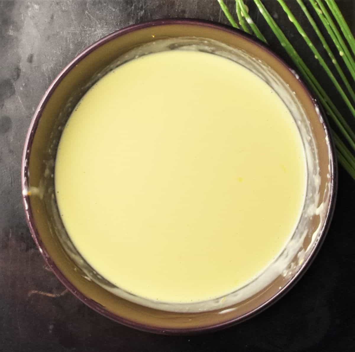 Creamy orange salad dressing in purple bowl with whisk in background.