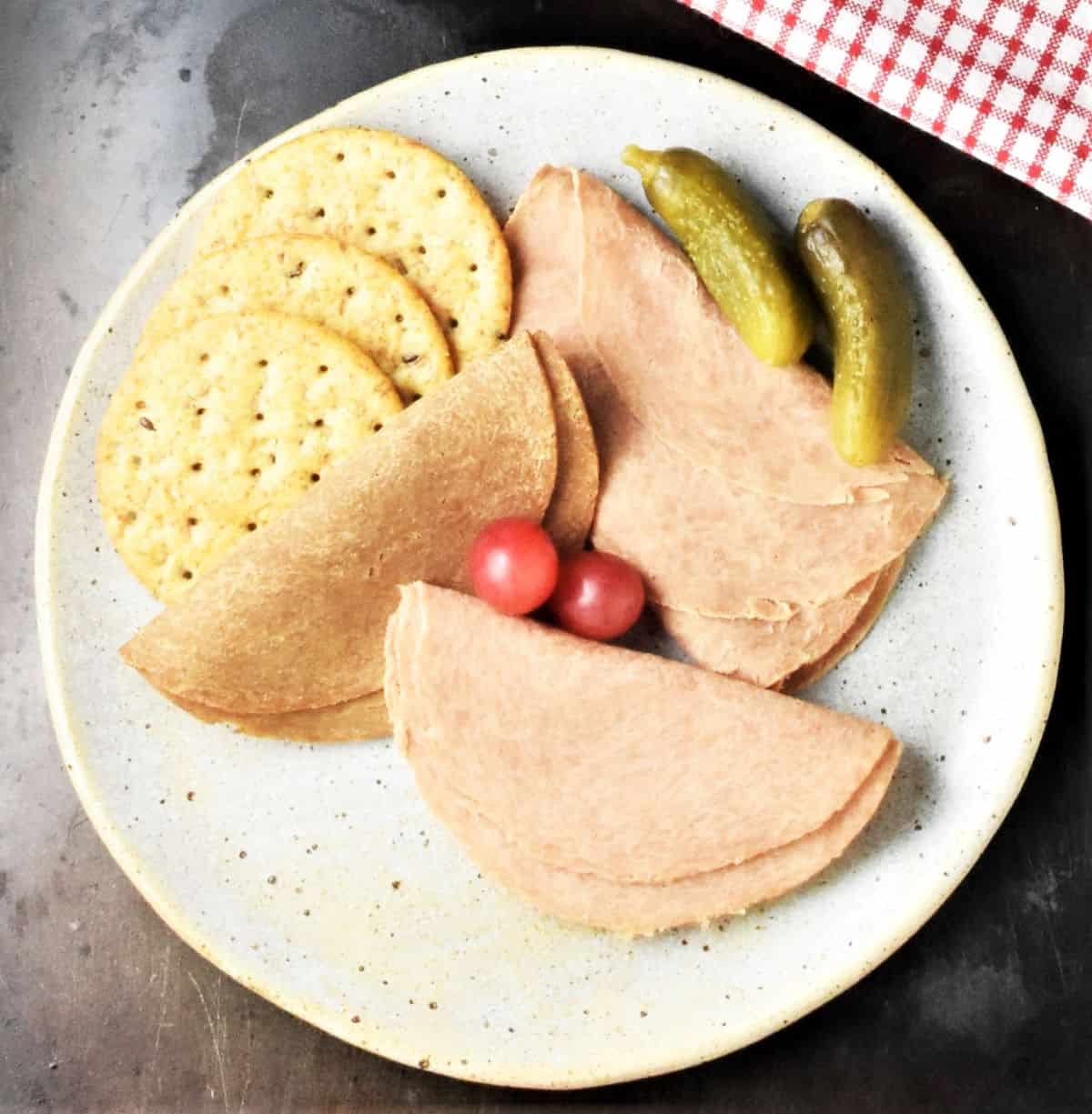 Deli slices with crackers on top of pplate.