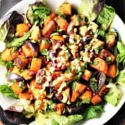 Top down view of roasted vegetable salad with creamy dressing on large white plate.