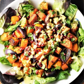 Top down view of roasted vegetable salad with creamy dressing on large white plate.