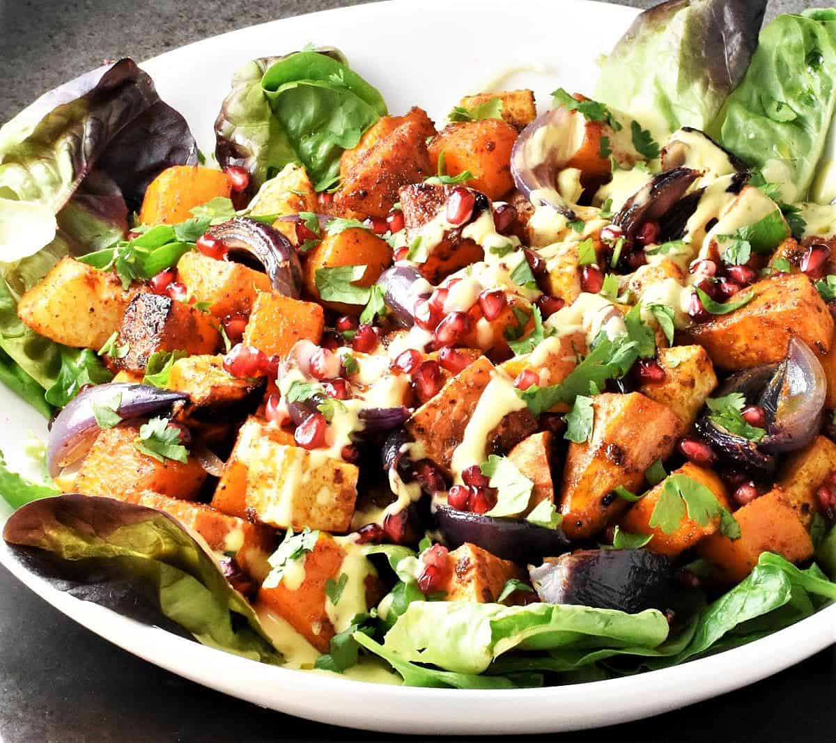 Close-up side view of salad with roasted vegetables and creamy dressing on white plate.