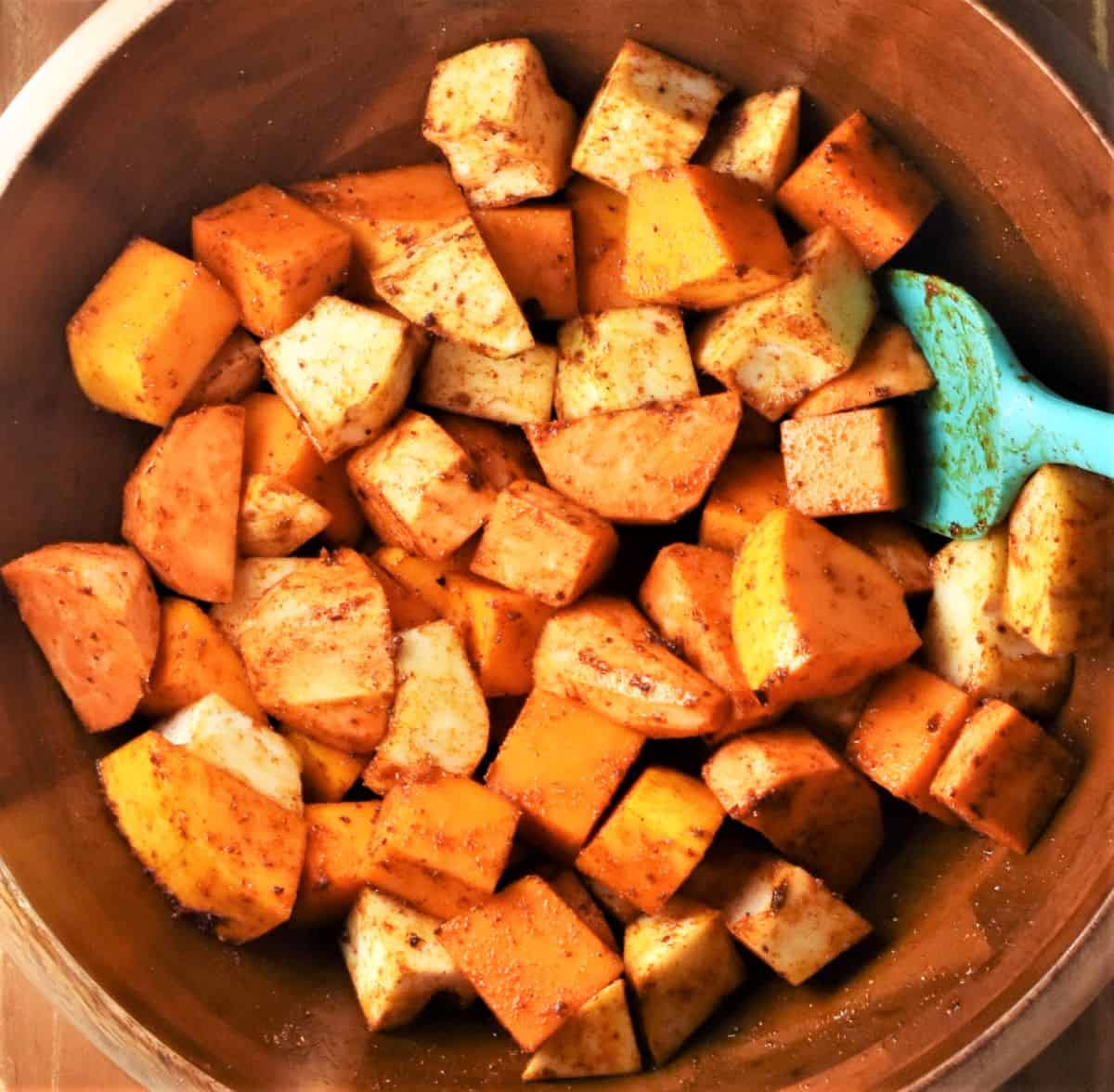 Cubed vegetables coated in spices with spoon in bowl.
