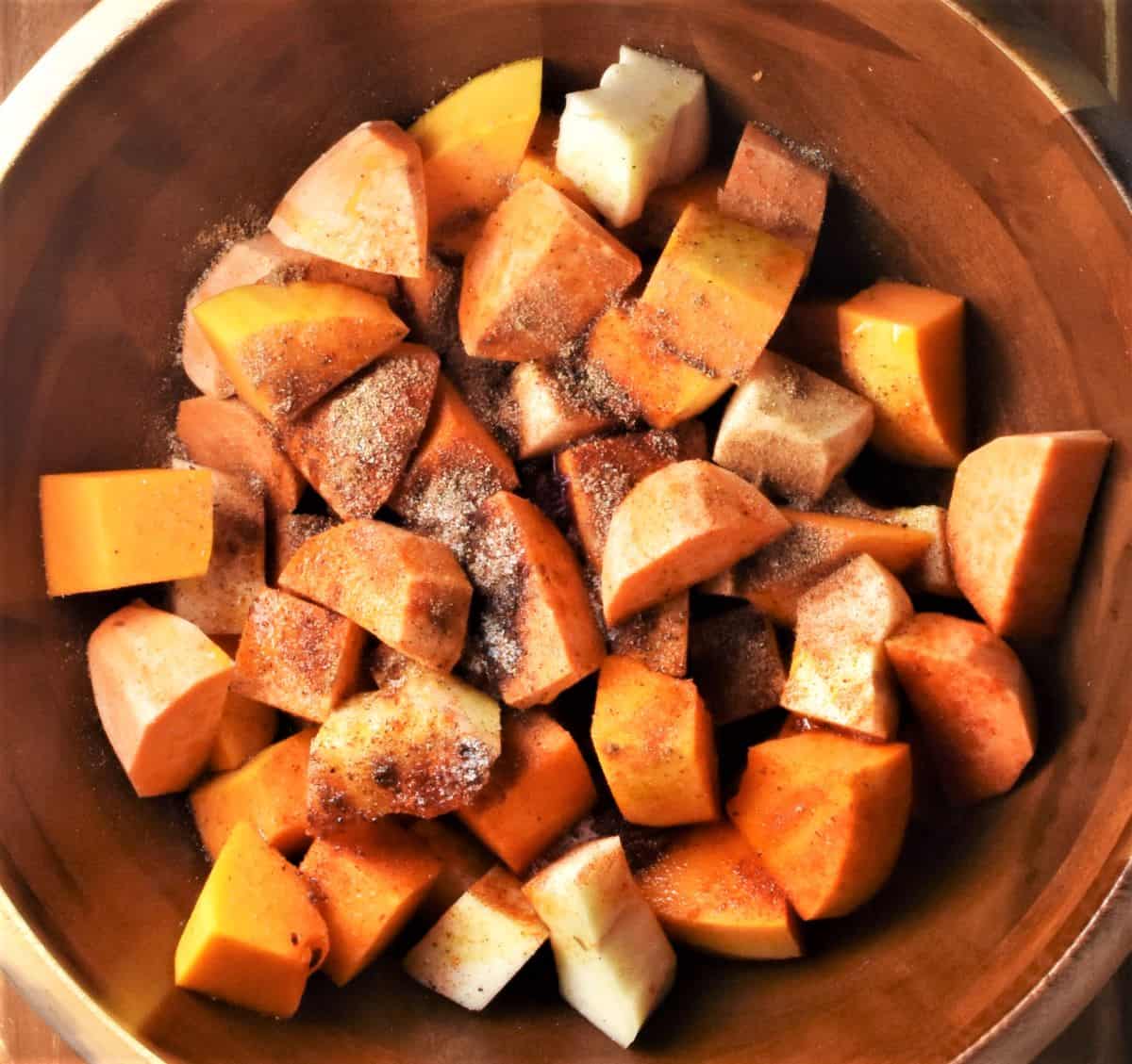 Cubed peeled vegetables with spices in mixing bowl.