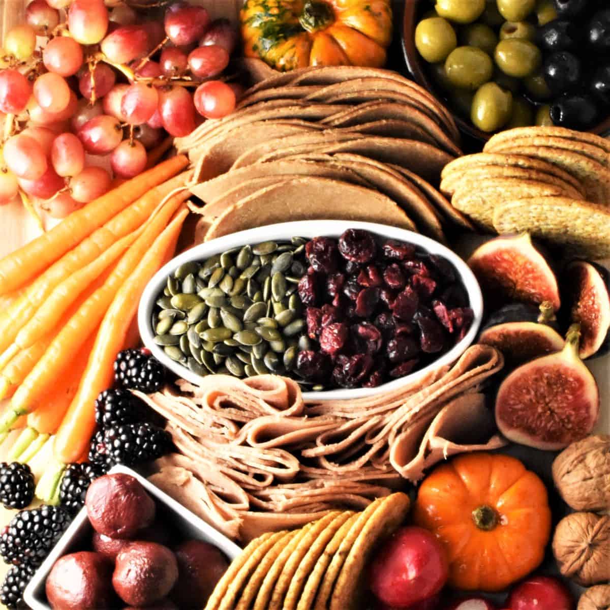 Vegan charcuterie board with meats, vegetables, fruits, crackers and seeds.