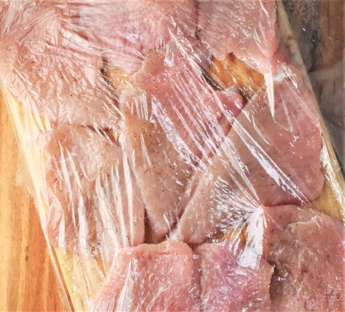 Turkey breast chops covered with plastic wrap.