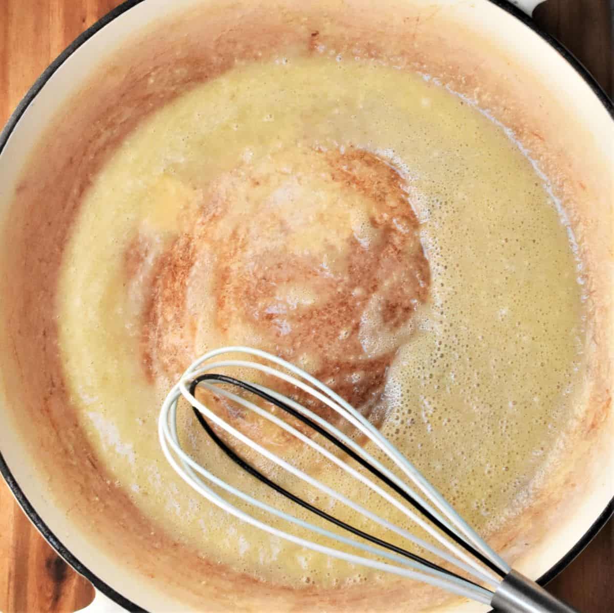 Creamy roux mixture in shallow pan with whisk.