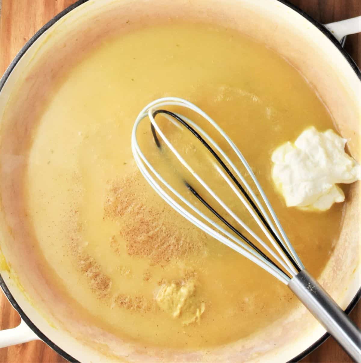 Creamy sauce with dollop of sour cream and whisk in shallow pan.