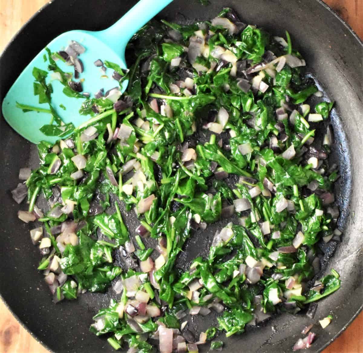 Onion and spinach mixture in large pan with blue spatula.