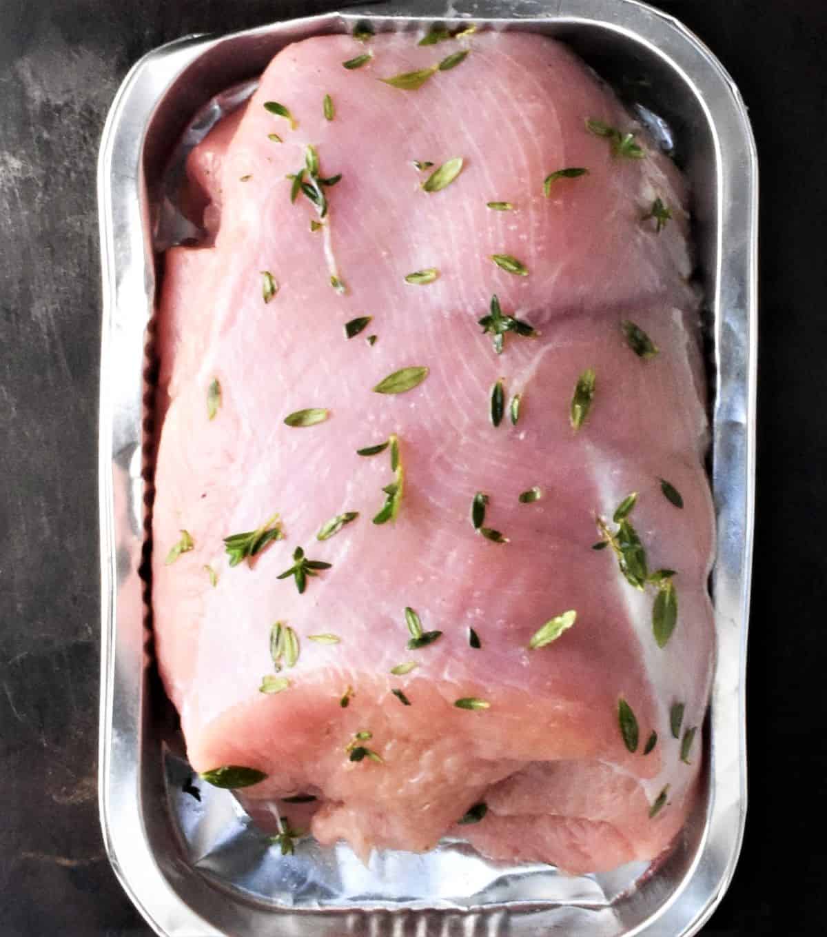Top down view of turkey breast with herbs in container.