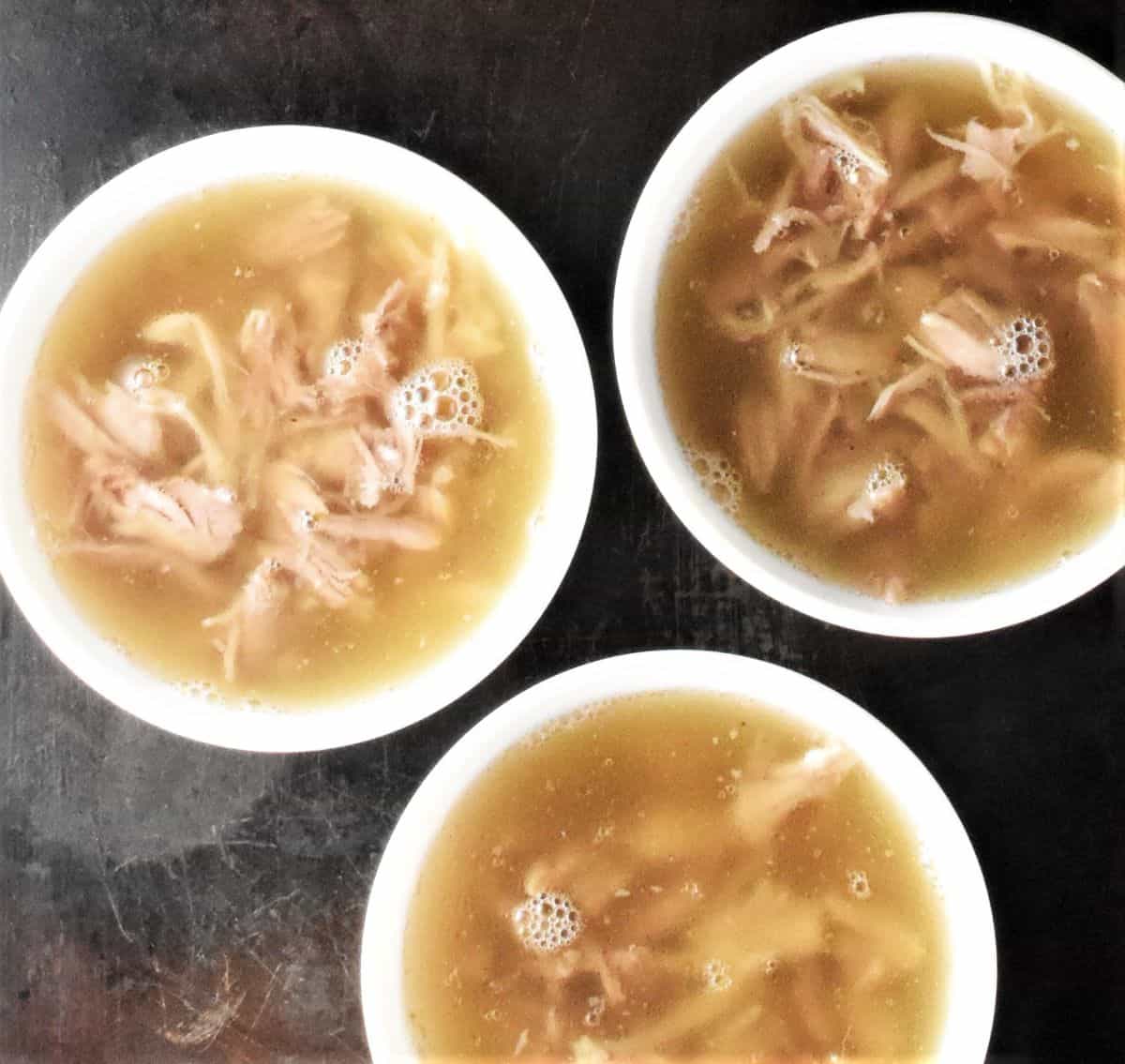 Top down view of meat jelly in 3 white bowls.