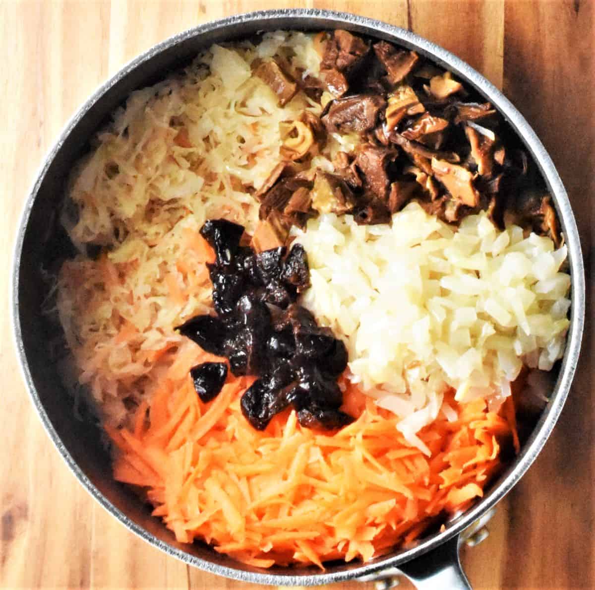 Sauerkraut with carrot, onion, prunes and mushrooms in pot.