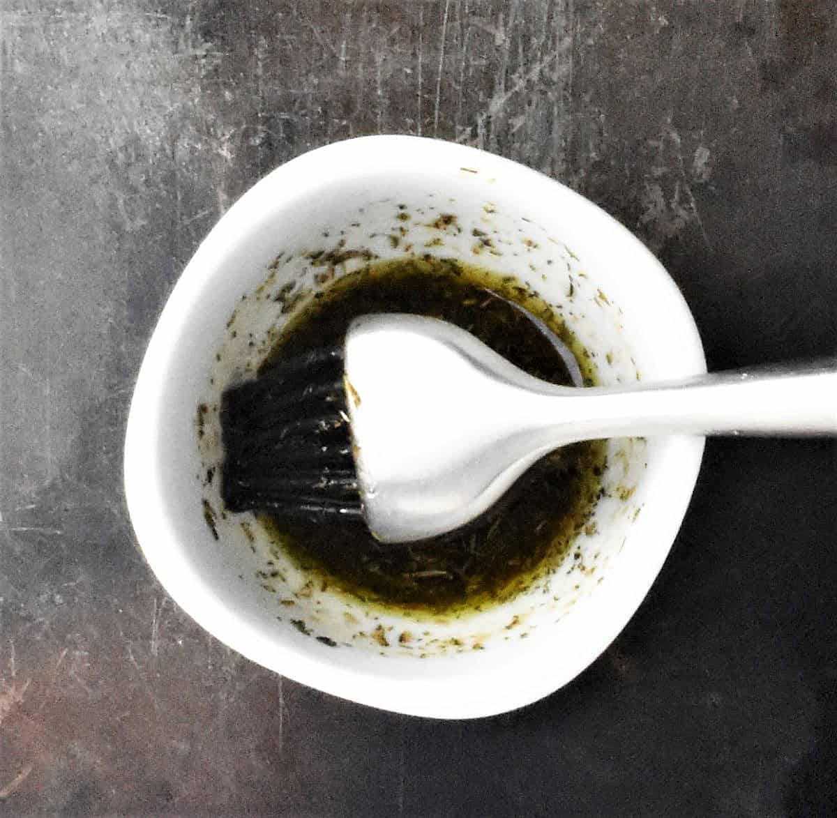 Top down view of balsamic dressing in white bowl with brush.