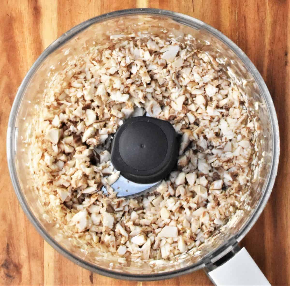 Top down view of finely chopped mushroom mixture in food processor bowl.