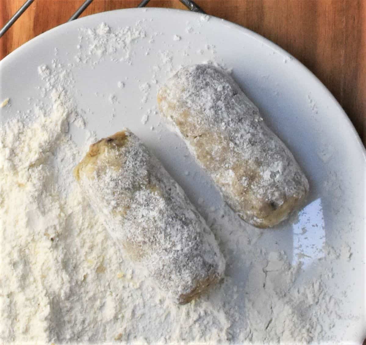 Coating croquettes rolls in flour on white plate.