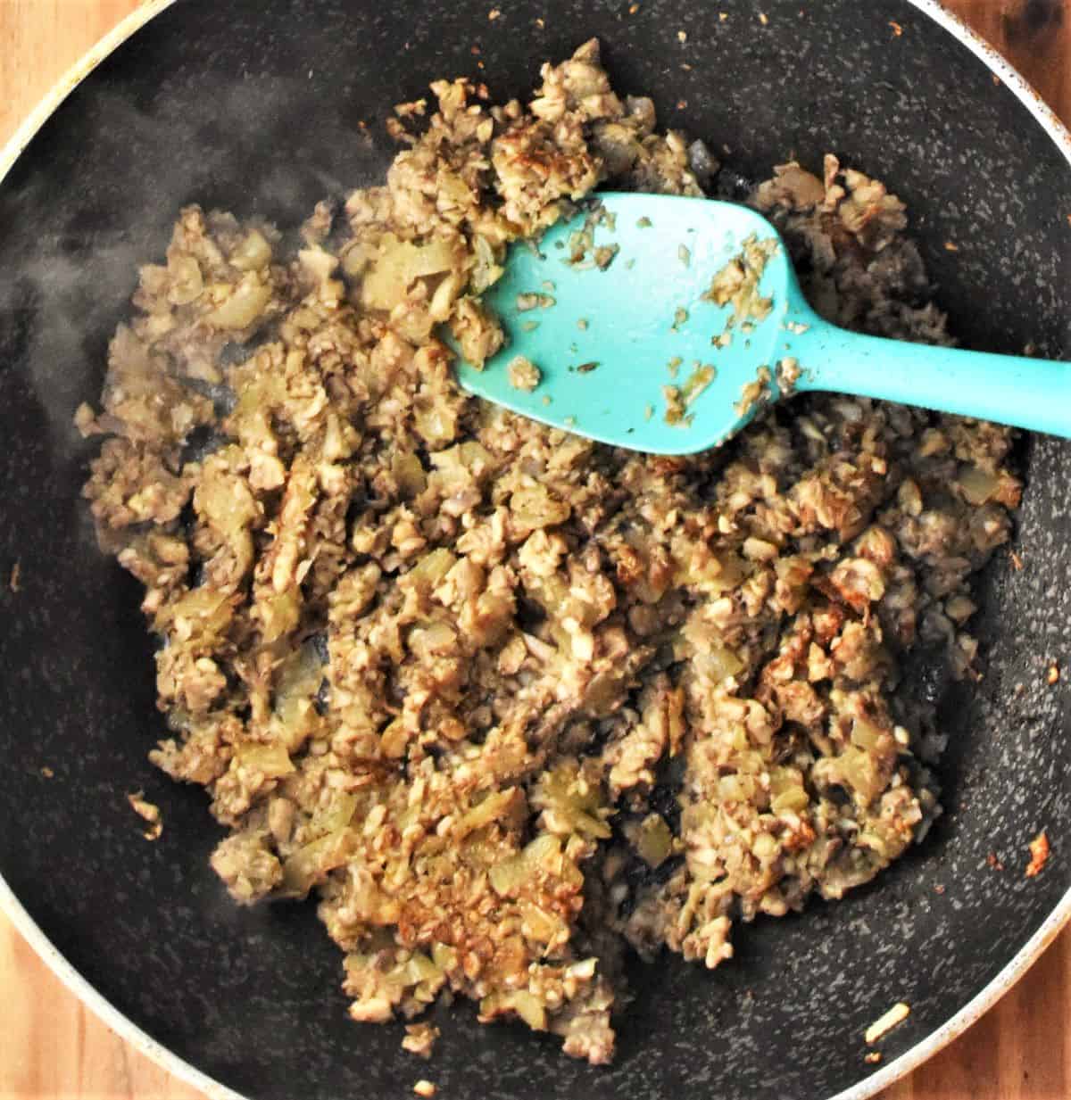 Mushroom filling mixture in pan with blue spatula.