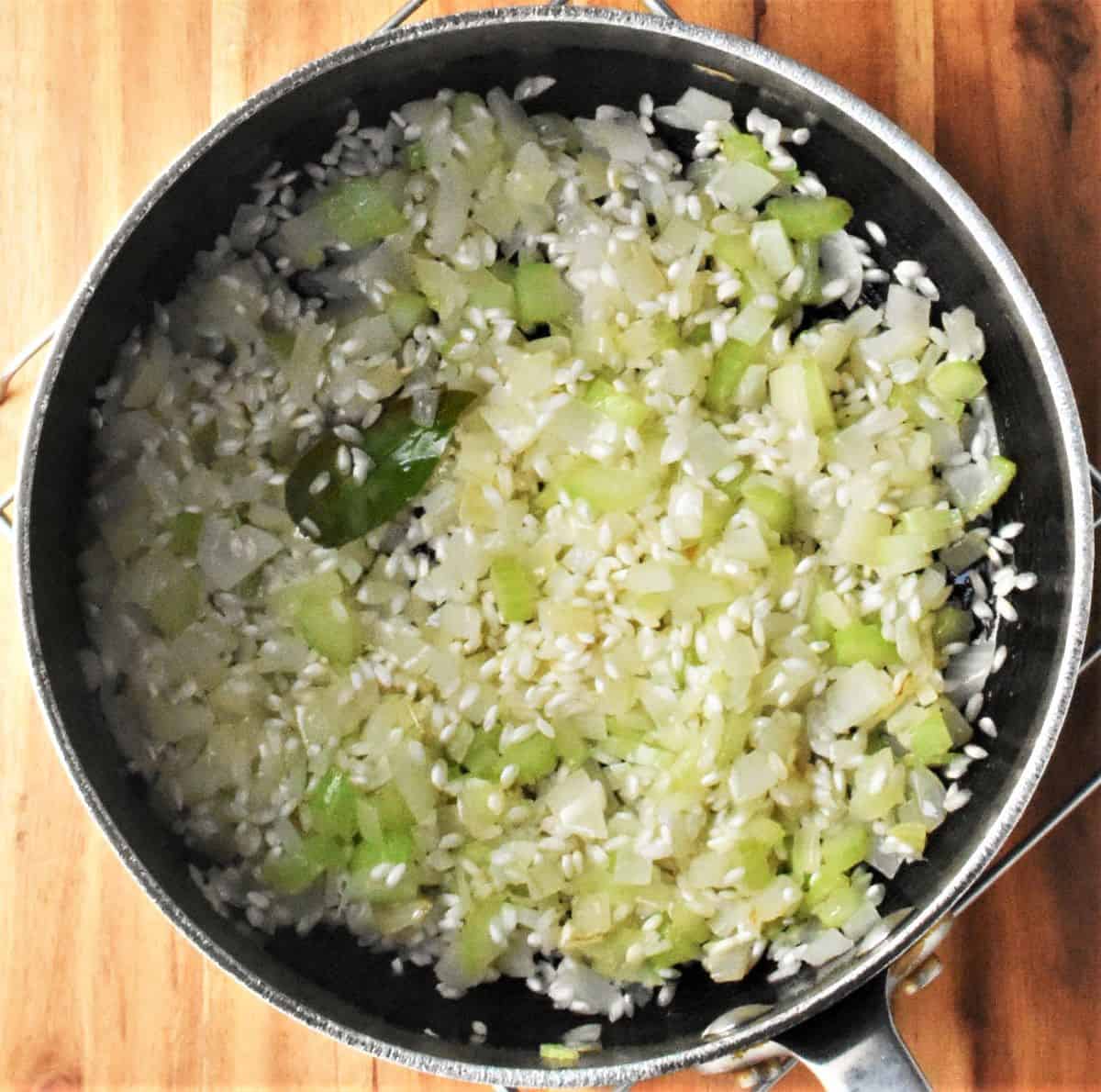 Cooking onion and rice with bay leaf in pot.