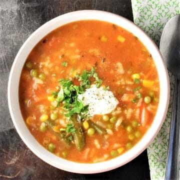 Top down view of vegetable rice soup with herb garnish and yogurt in white bowl.