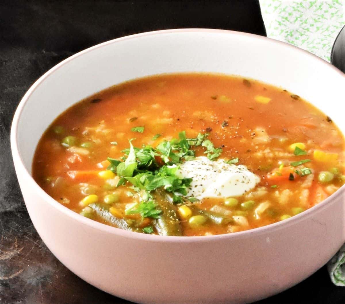 Close-up side view of rice vegetable soup in white bowl.