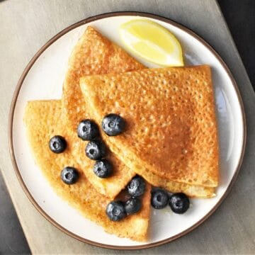 Top down view of 3 folded buckwheat crepes with blueberries and lemon wedge on plate.