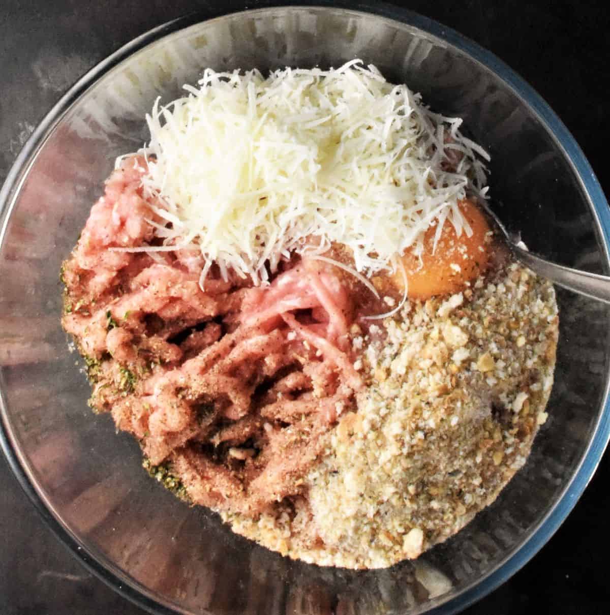 Top down view of ground chicken, grated cheese, egg and breadcrumbs in bowl.