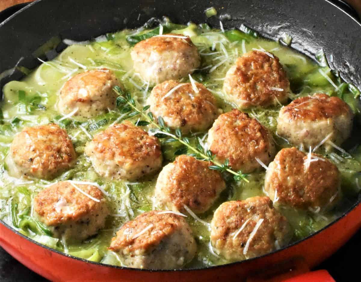 Side view of meatballs in leek sauce in pan.