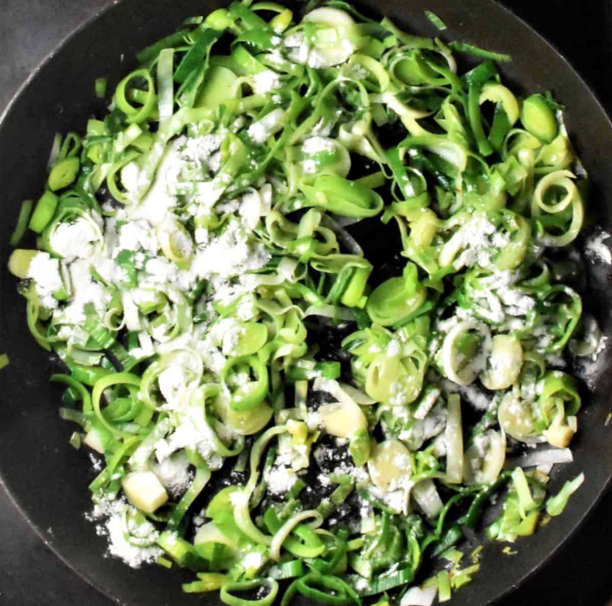 Cooking sliced leeks with flour in pan.