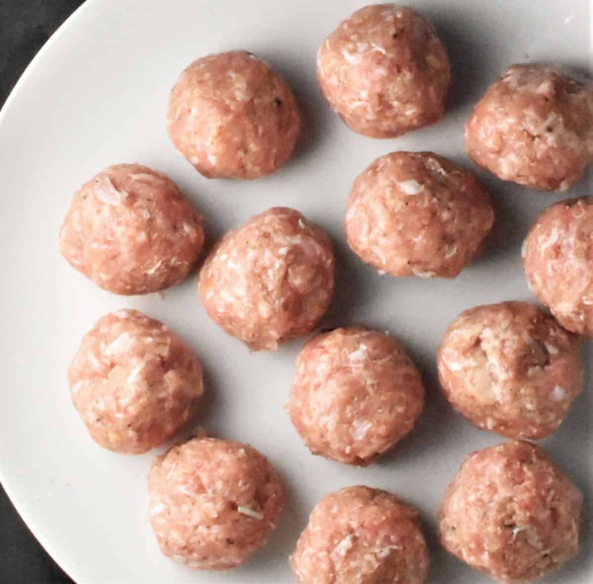 Raw meatballs on top of white plate.