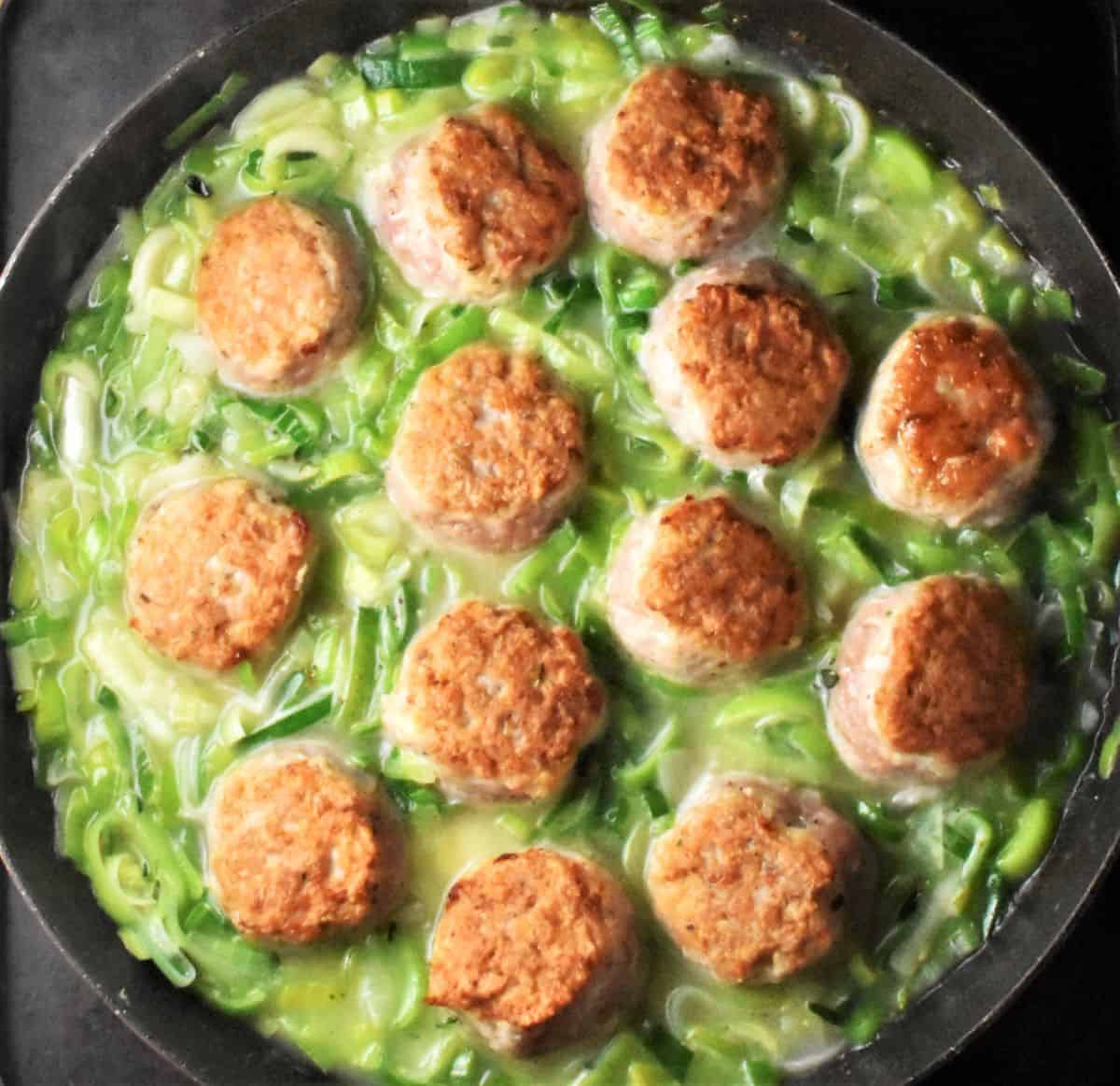 Meatballs in leek sauce in pan.