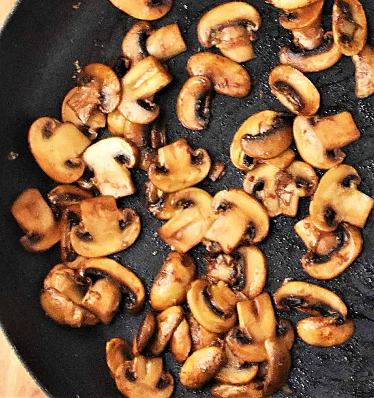 Top down view of browned slices of mushrooms in large skillet.