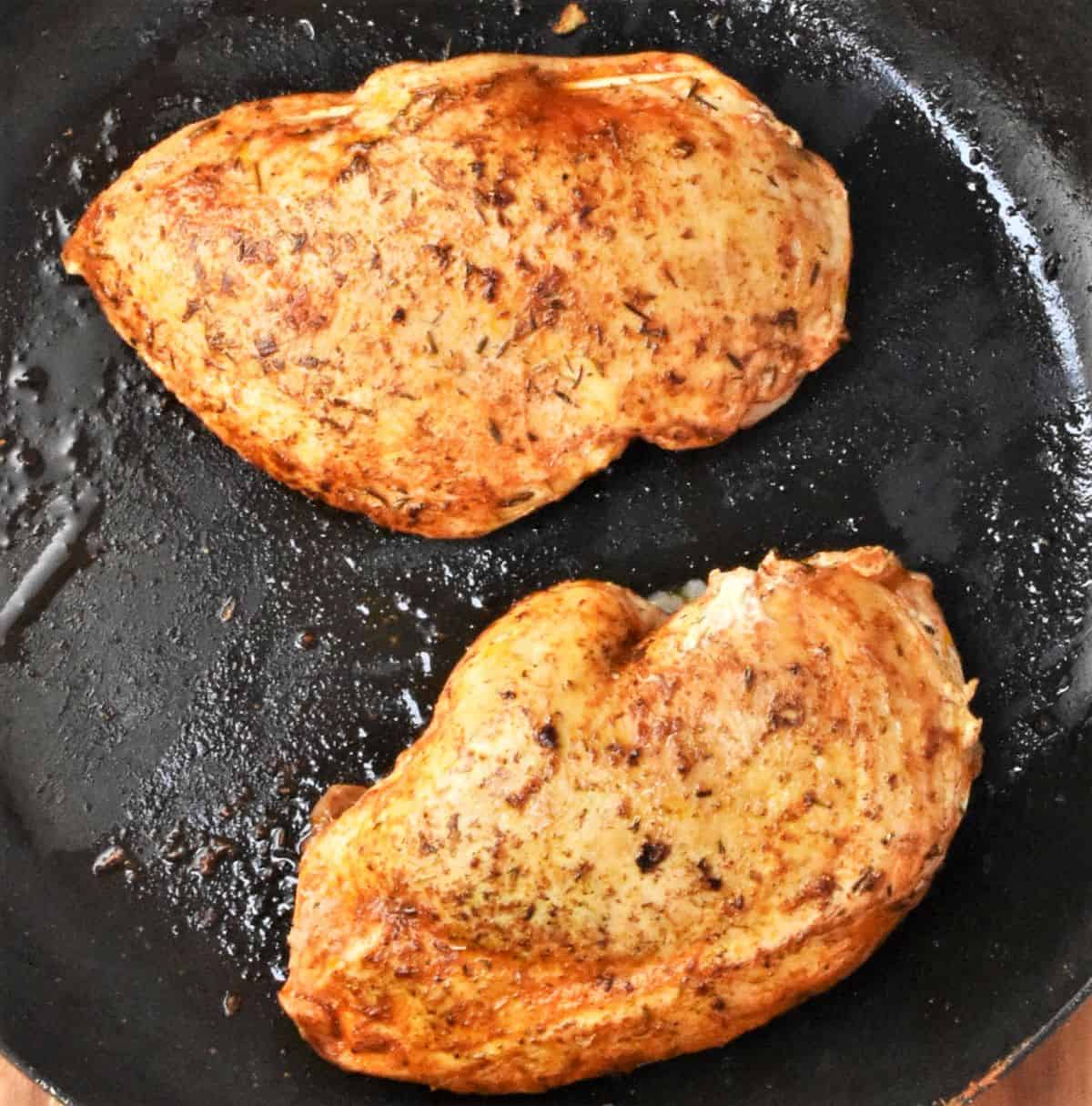 Top down view of frying 2 chicken breasts in pan.