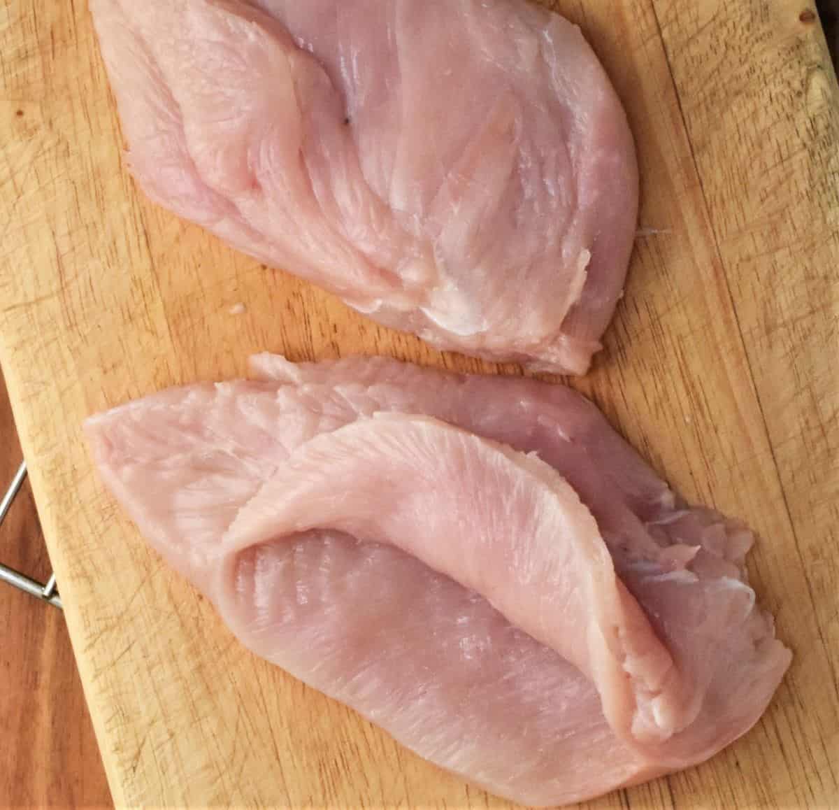 2 skinless chicken breasts on top of cutting board.