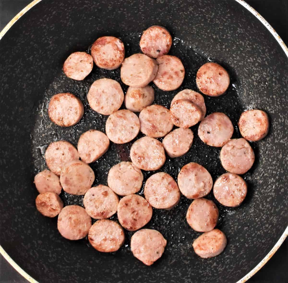 Top down view of kielbasa slices lightly browned in pan.