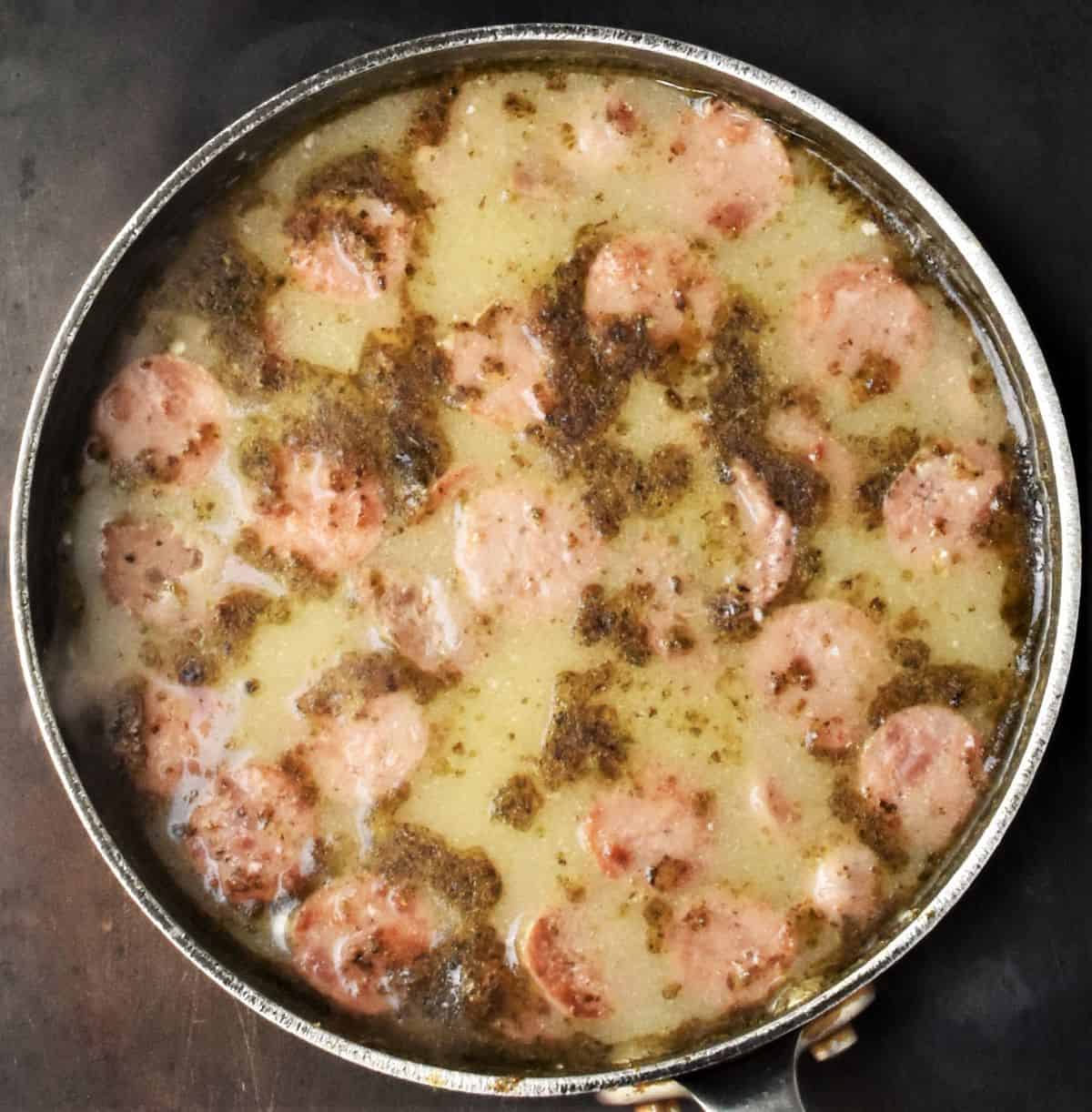 Top down view of soup in pot with herbs and sausage pieces floating at the top.