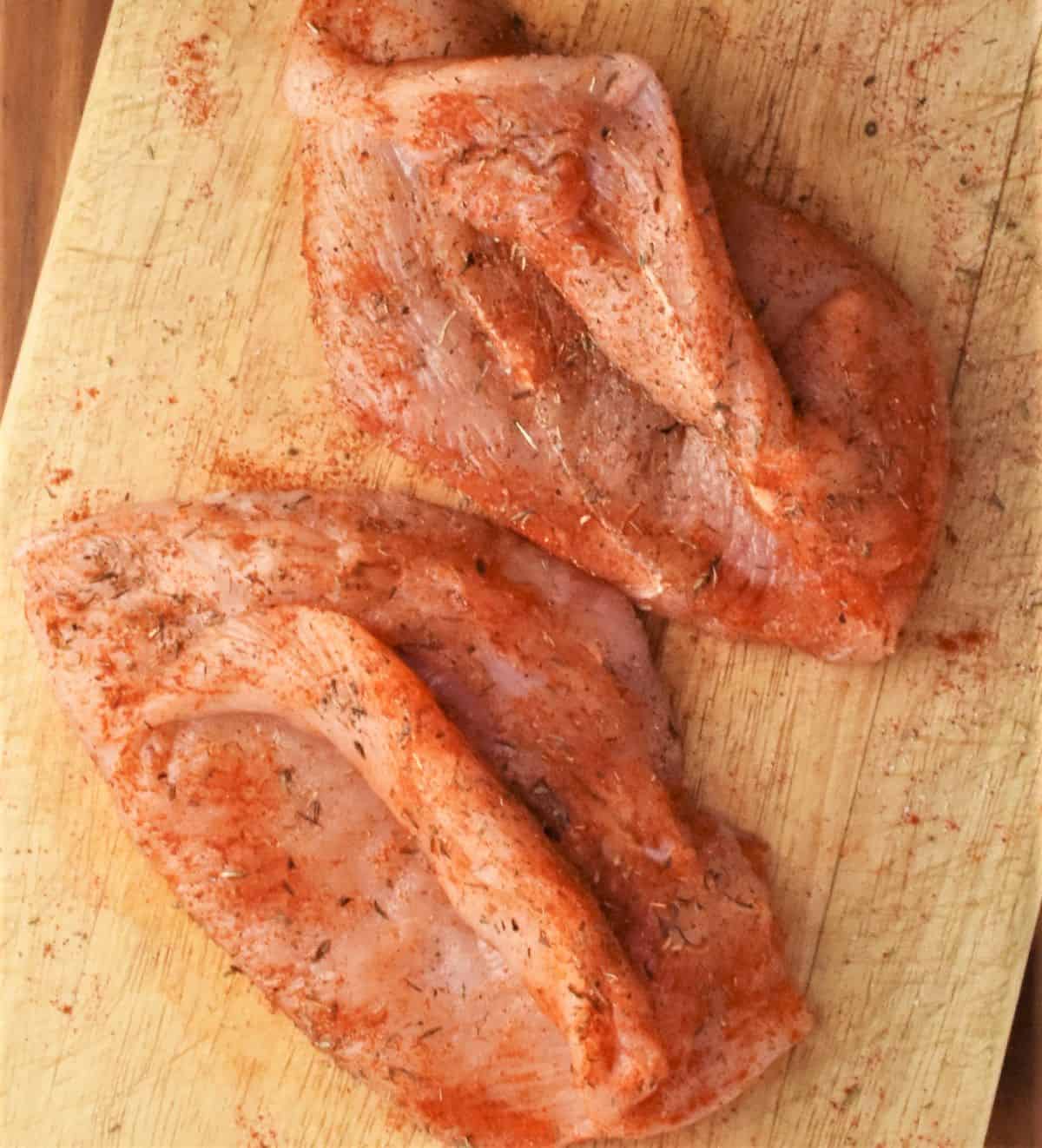 2 seasoned chicken breasts on cutting board.