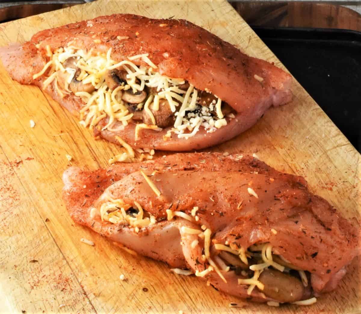 Side view of stuffed raw chicken breasts on cutting board.