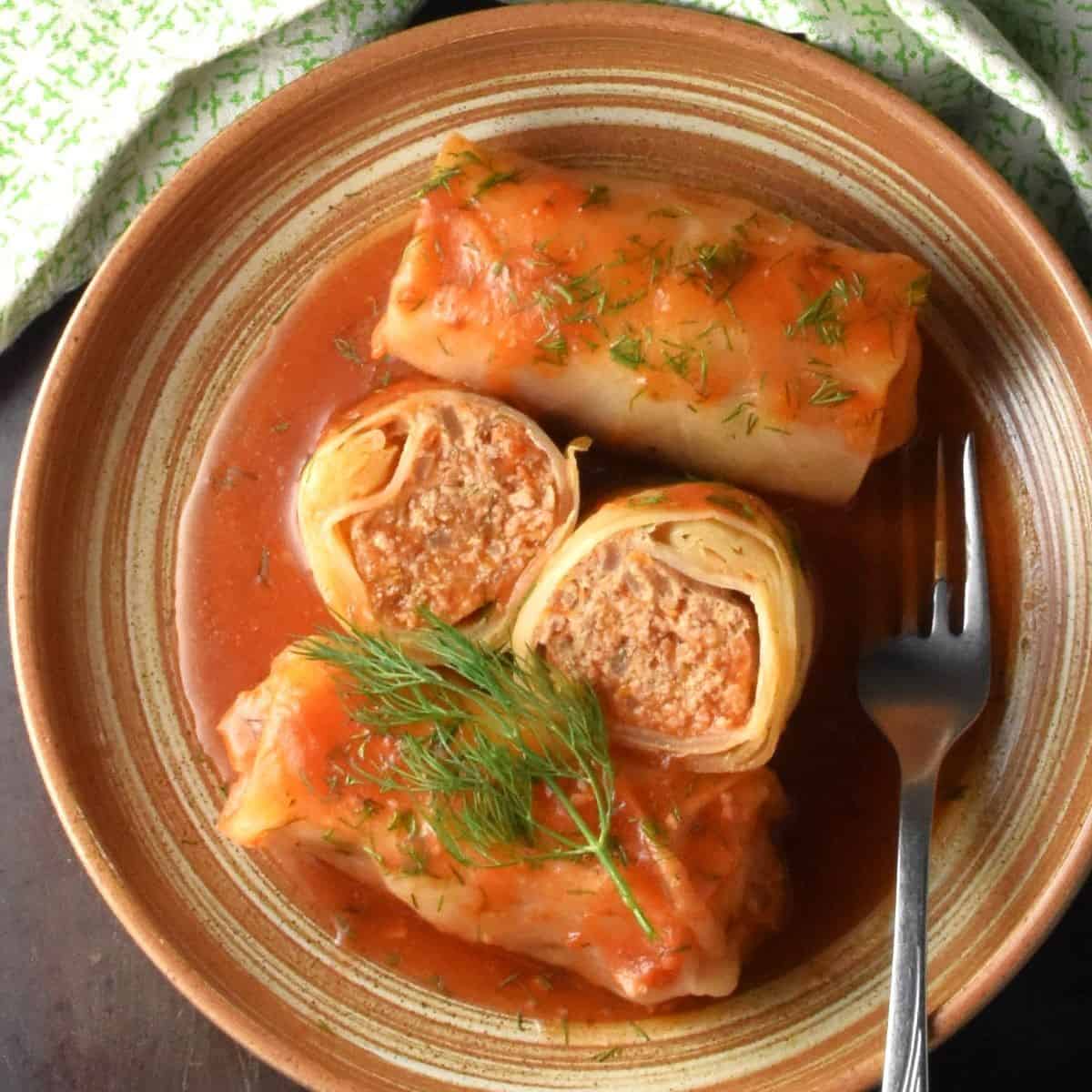 Top down view of turkey cabbage rolls with tomato sauce in brown bowl with fork.