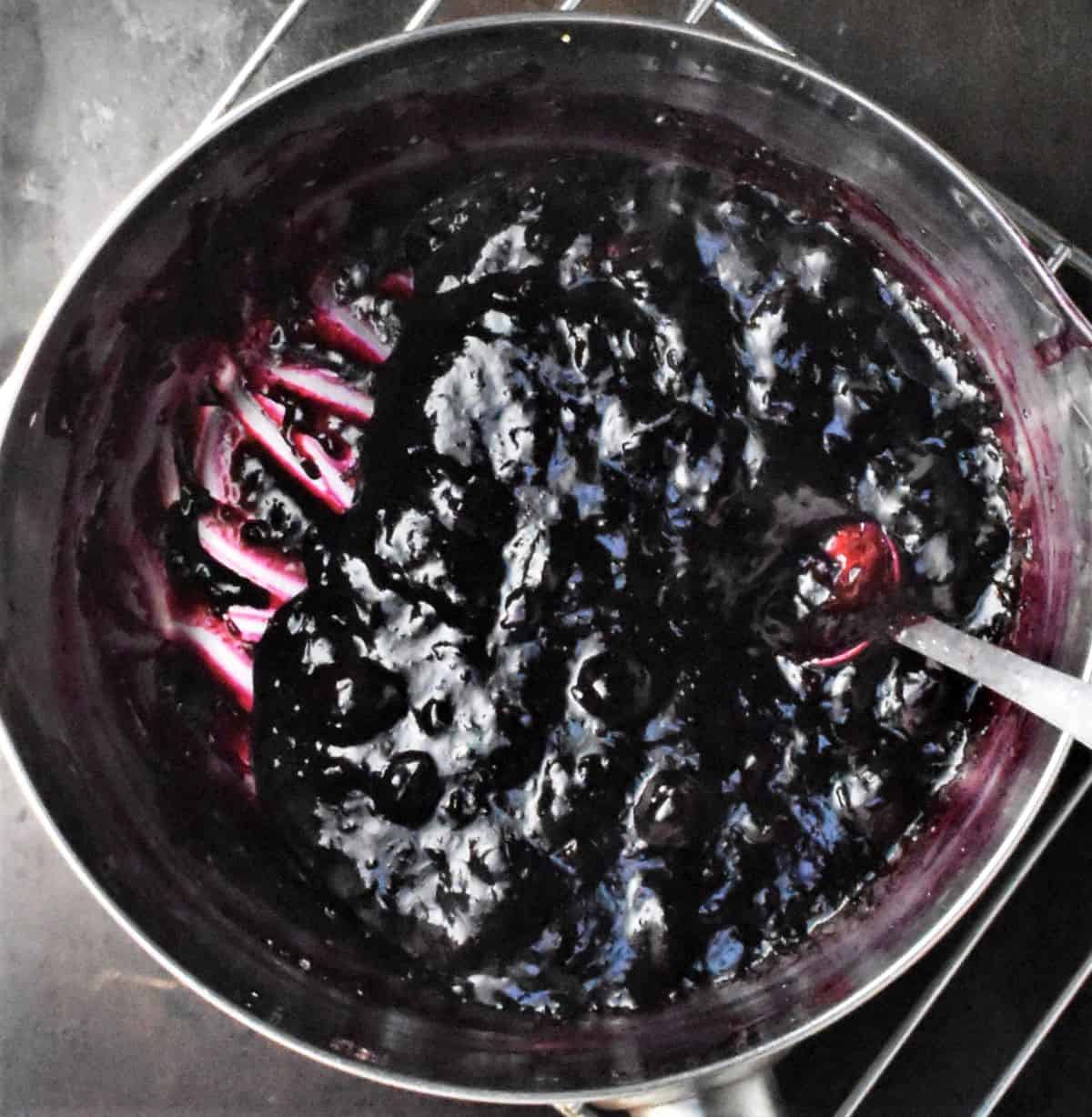 Top down view of thick blueberry mixture with spoon in saucepan.