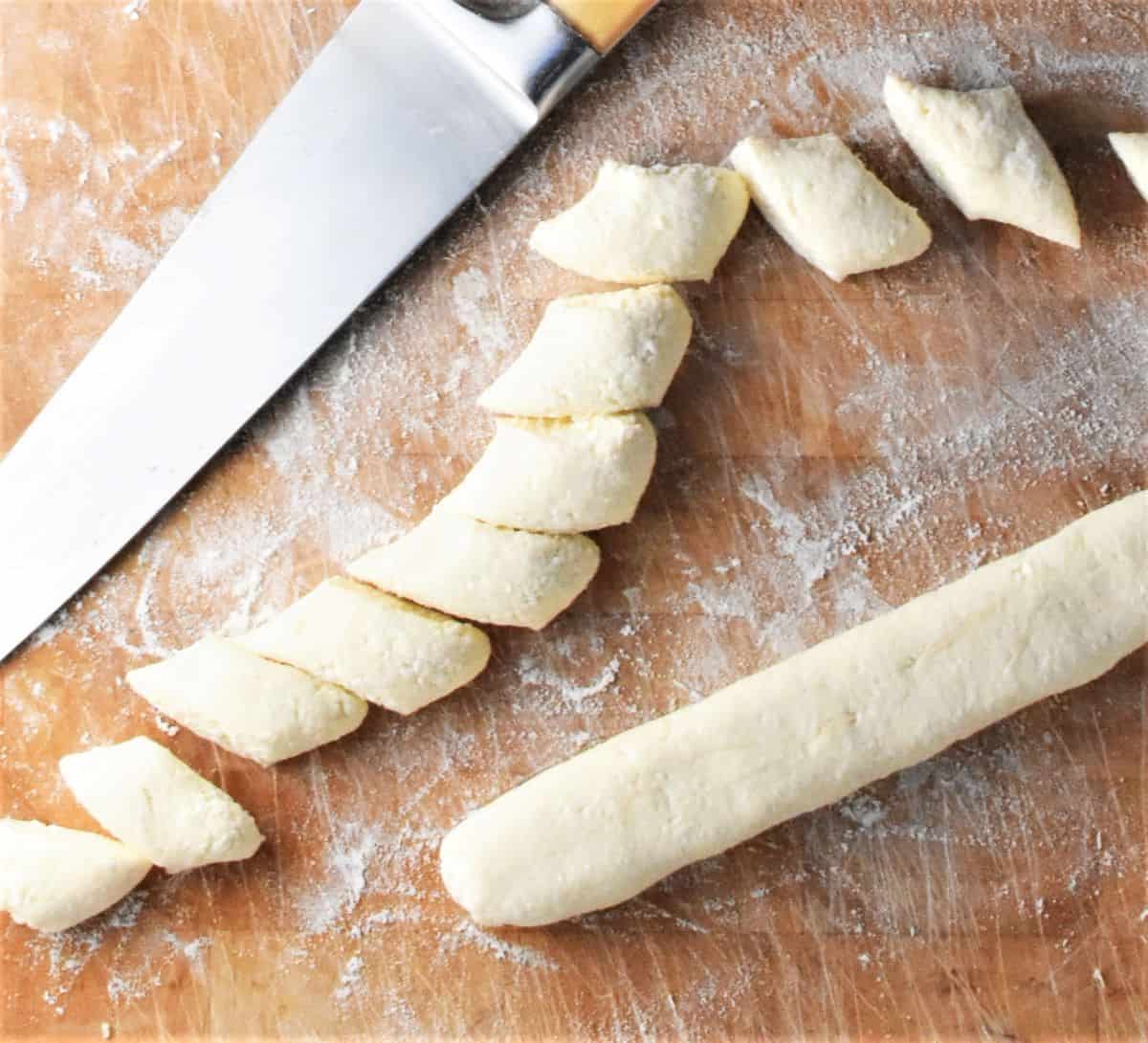 Cutting lazy dumpling dough into small pieces with knife on top of wooden board.