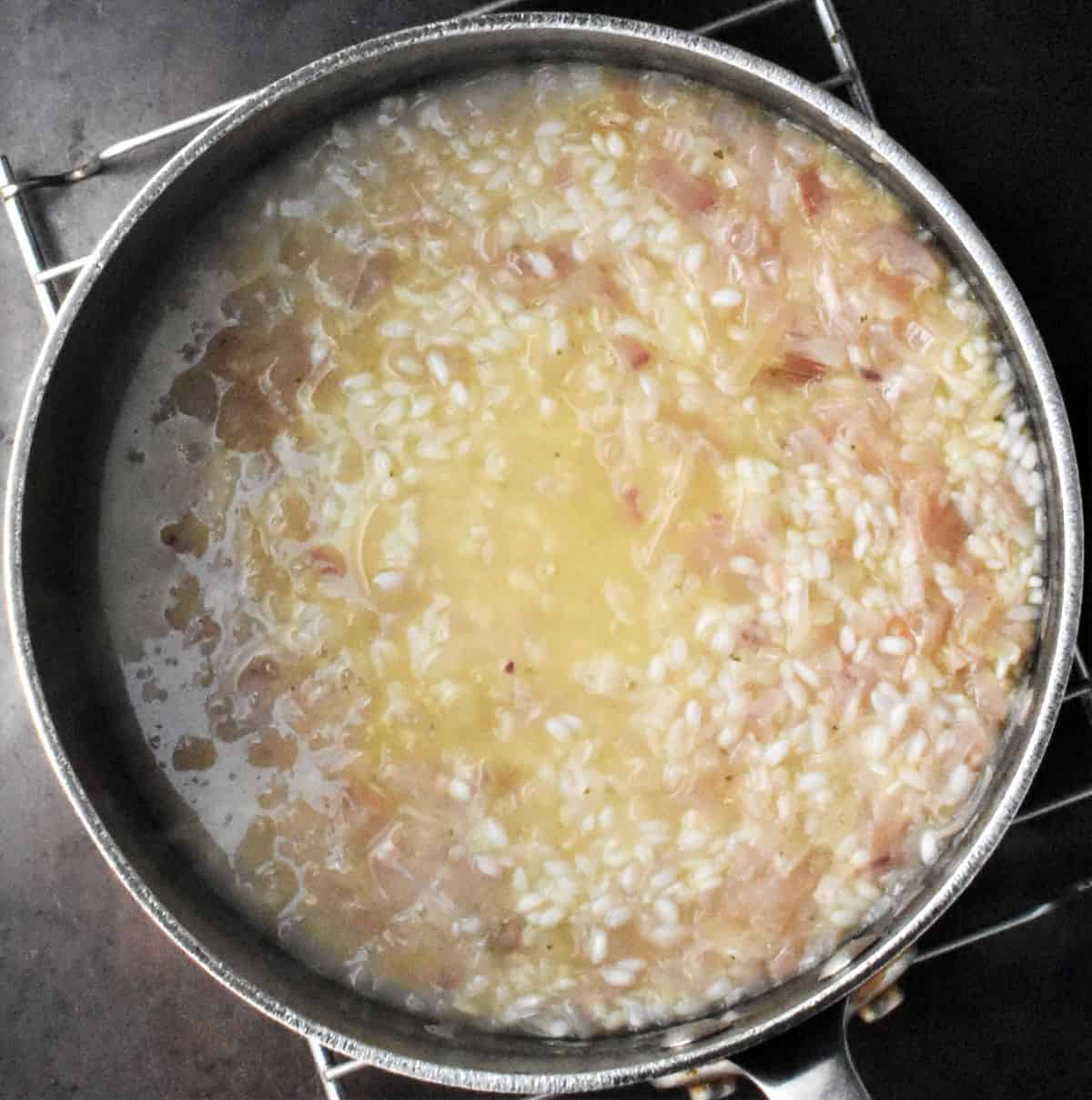 Top down view of risotto rice with stock in large pot.