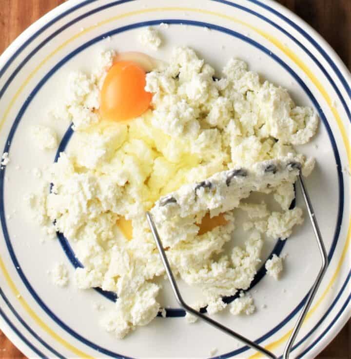 Twarog cheese mixture with egg and potato masher in bowl.