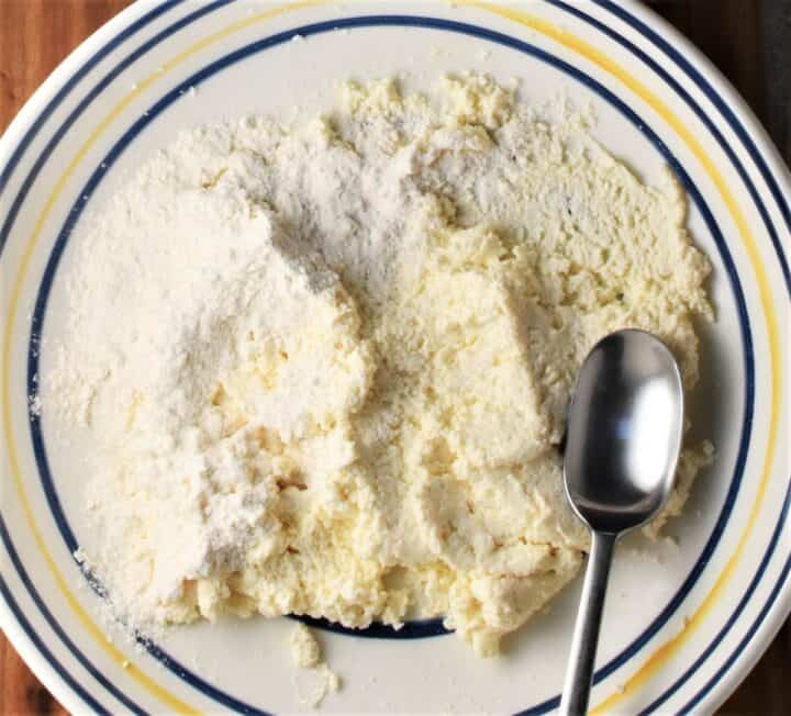 Twarog with flour and spoon in bowl.