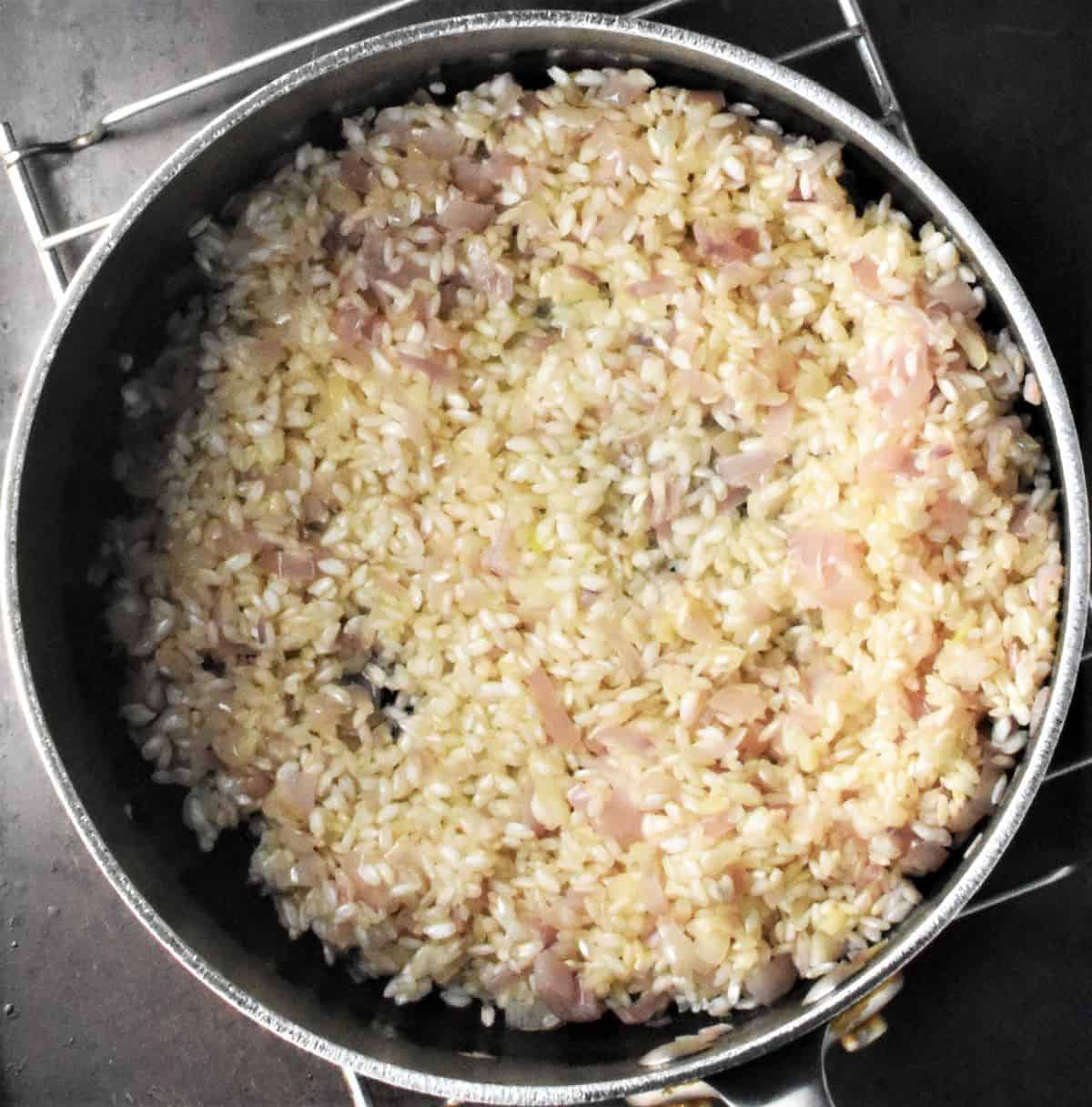 Top down view of risotto rice with shallots in pot.