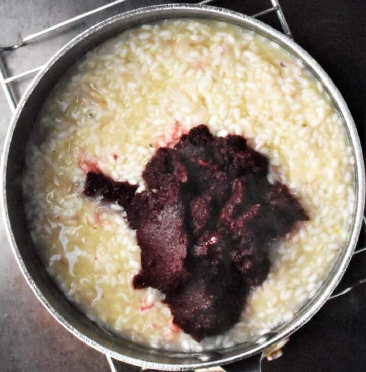 Creamy risotto with beet puree in pot.