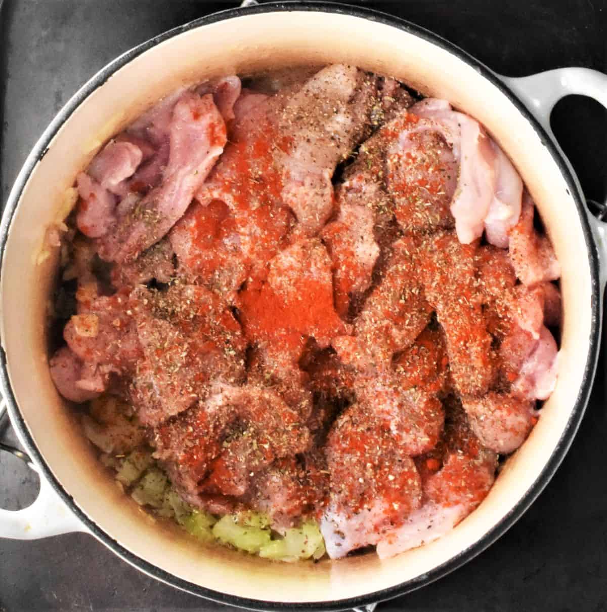 Chicken pieces with spices in large white pot.